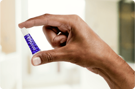 A hand holding a small tube of Eroxon, the product's branding visible.