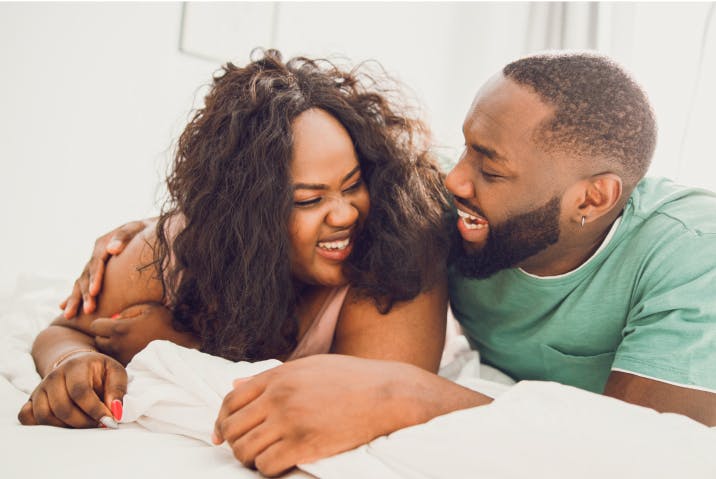 Joyful couple in bed, man whispering something funny to his partner.