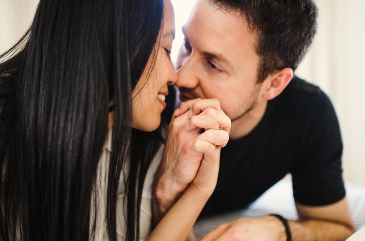 A couple leaning in close, holding hands and smiling at each other.