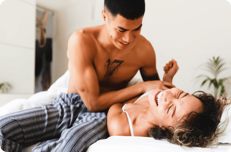 Man and woman playful on a bed, both smiling broadly
