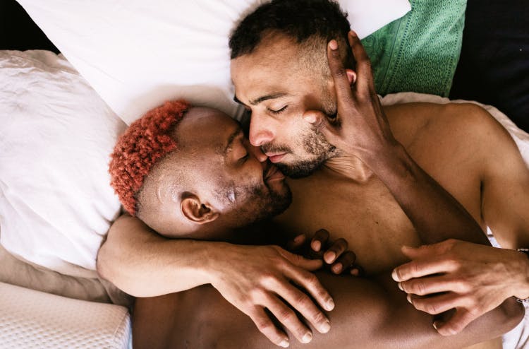 Two men lying in bed, holding each other closely and sharing an intimate moment.