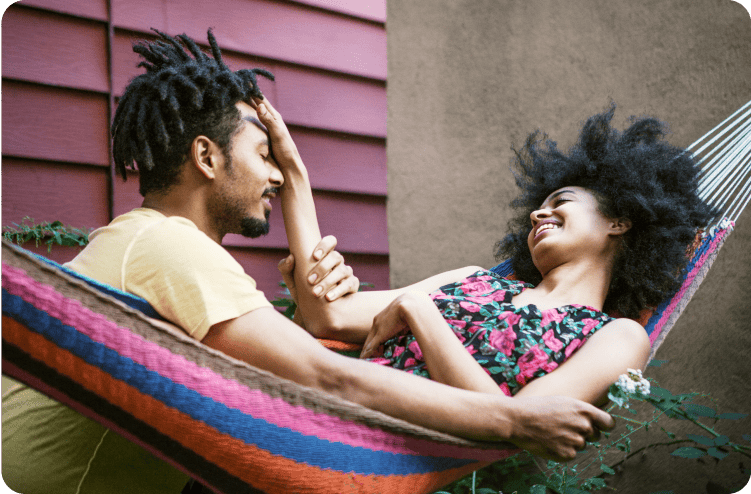 A couple relaxing in a hammock, smiling and enjoying each other’s company outdoors.