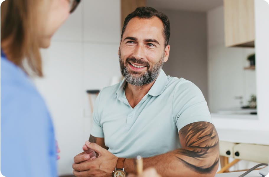 Bearded man with tattoos, smiling at a woman in a bright kitchen