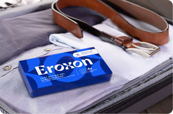 An open suitcase with clothes, a smartphone, and a box of Eroxon inside, ready for travel.